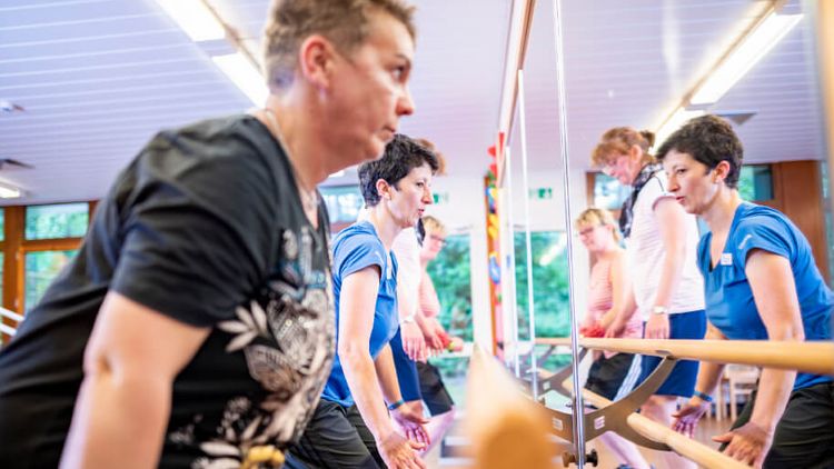 Patientengruppe trainiert in der Physiotherapie vor einem großen Spiegel