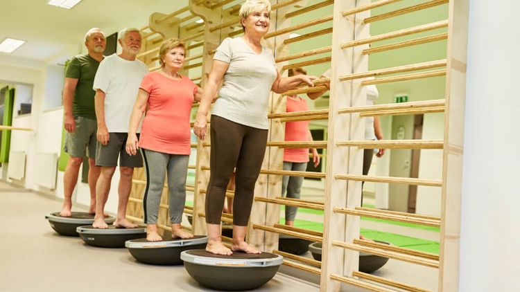 Eine Gruppe Senioren trainiert ihr Gleichgewicht in der Turnhalle auf dem Bosu Ball