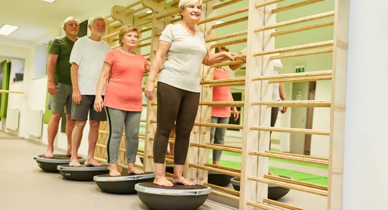 Eine Gruppe Senioren trainiert ihr Gleichgewicht in der Turnhalle auf dem Bosu Ball