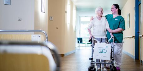 Pflegekraft begleitet ältere Patientin durch den Flur