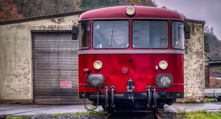 Roter Schienenbus steht vor kleinem Lokschuppen