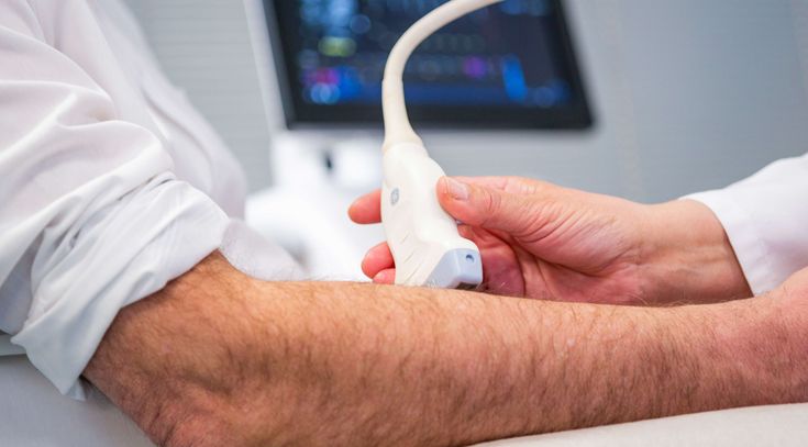 Ärztin untersucht Arm eines Patienten mit Ultraschall