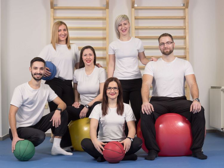 Gruppenbild Therapeutinnen und Therapeuten in weißen T-Shirts mit Bällen vor einer Sprossenwand