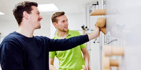 Lächelnder Patient trainiert zusammen mit Therapeuten in der medizinisch-beruflich orientierten Rehabilitation