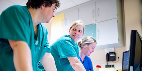 Drei Pflegekräfte im Stationszimmer planen die Schichtübergabe