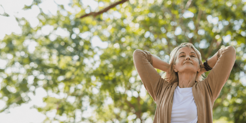 Blonde Frau genießt den Sonnenschein vor einem herbstlichen Baum