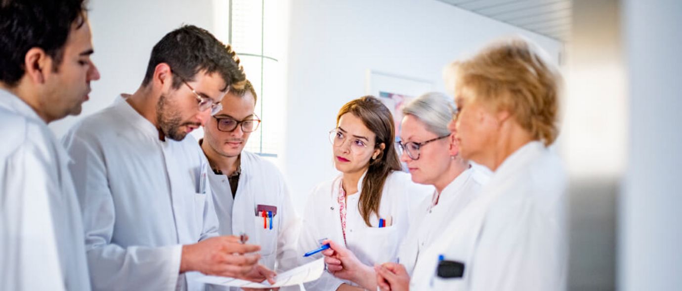 Eine Gruppe männlicher und weiblicher Ärzte diskutiert über eine Patientenakte