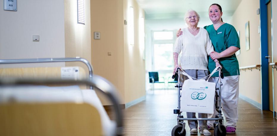 Weibliche Pflegekraft geht mit älterer Patientin durch den Krankenhausflur