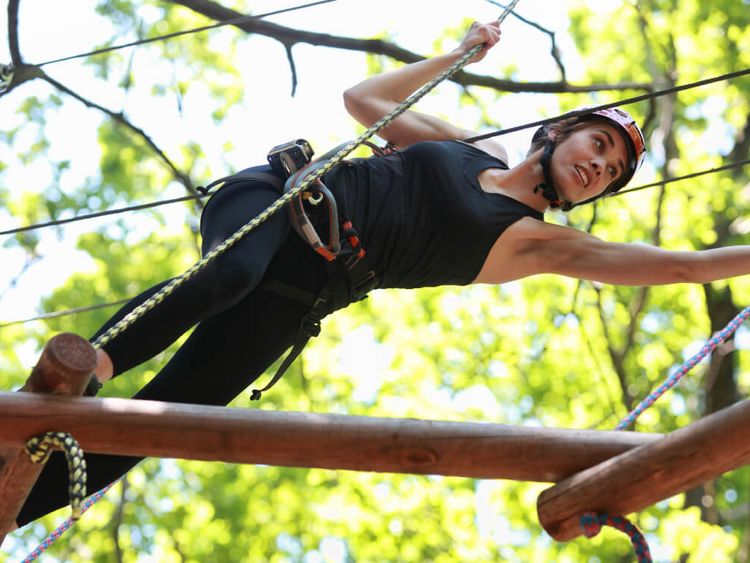 Junger Mann mit Helm klettert im Kletterpark zwischen den Bäumen