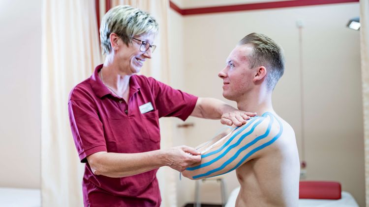 Therapeutin legt Patienten Kinesio-Taping an