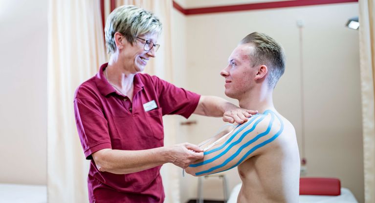 Therapeutin legt Patienten Kinesio-Taping an