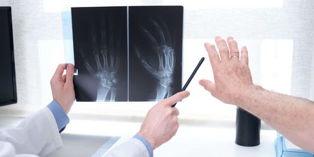 Arzt erklärt Patienten Röntgenbild einer Hand auf dem Computermonitor